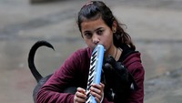 Nuran duduk sambil memainkan pianika di atas jalan yang basah karena hujan (Foto: Dok. Mahmut Serdar Alaku?/Anadolu Agency)