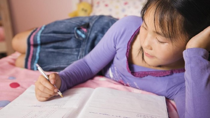 Girl with homework on bed