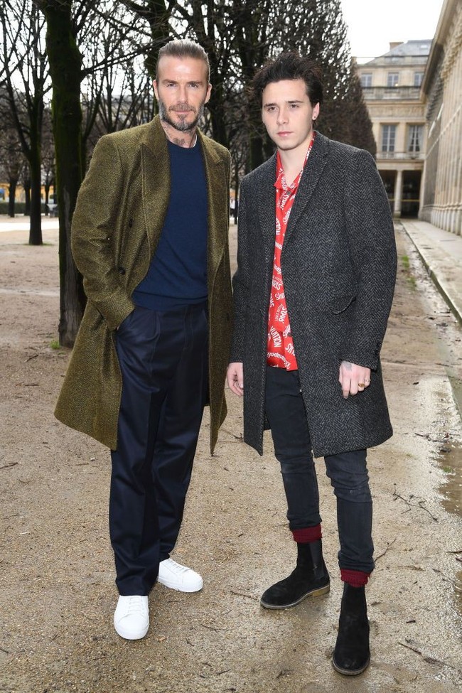 Brooklyn Beckham pun mencuri perhatian berbalut kemeja merah bertulisan Louis Vuitton. Ia melengkapi penampilannya dengan coat abu-abu. Foto: Getty Images