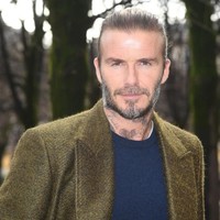 David Beckham tak kalah stylish, ia memilih baju berpalet gelap dengan mantel olive green sebagai outerwear. Foto: Getty Images