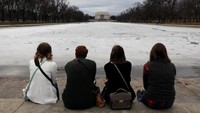 Beberapa pengunjung lainnya tampak duduk di dekat kolam yang ada di seberang Lincoln Memorial. Kolam itu tengah diselimuti es tebal karena musim dingin masih menyelimuti AS. Foto: REUTERS/Yuri Gripas