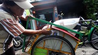Seorang tukang becak menunjukan stiker yang ditempel di becaknya.