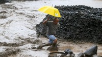 Seorang bapak yang membawa payung warna kuning ini nampak susah payah menyebrangi sungai yang diterjang banjir lahar dingin. Foto: REUTERS/Romeo Ranoco