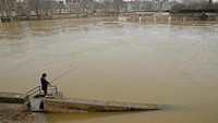 Seorang warga tempak sedang memancing di tepi Sungai Seine, Sabtu (27/1/2018). Sungai Seine terpantau meluap beberapa hari terakhir dan menyebabkan banjir di kawasan sekitarnya. (Foto: Dok. REUTERS/Pascal Rossignol)