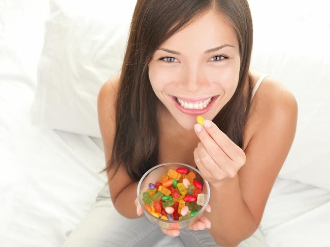 Candy woman eating sweets with a fresh smile in bed - copy space. Top view of Mixed Chinese Asian / Caucasian model. Click for more: