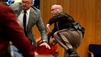 Nassar yang berbaju tahanan warna oranye tampak dilindungi oleh salah satu deputi sheriff setempat. Dia lalu digiring keluar ruang sidang. Foto: REUTERS/Rebecca Cook