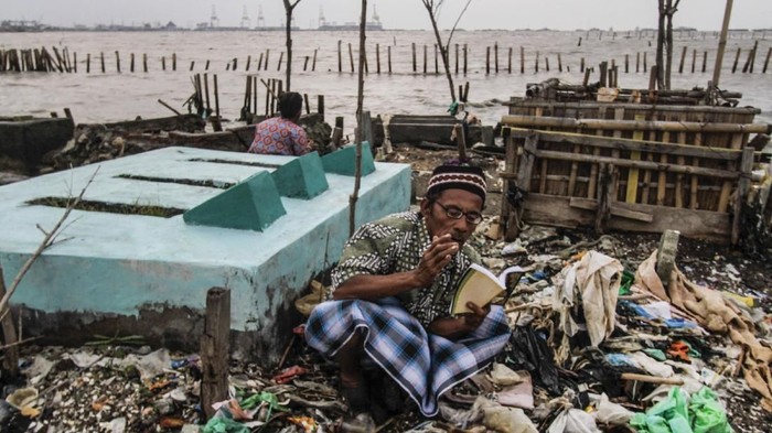 SEMARANG, INDONESIA – 2 FEBRUARY: Seorang warga berdoa di depan makam yang dipenuhi sampah akibat banjir luapan air laut di kawasan Desa Tambak Lorok, Semarang, Jawa Tengah pada 2 Februari 2018. Berdasarkan data Dinas Kelautan dan Perikanan setempat, tingginya gelombang abrasi pantai yang dipicu semakin berkurangnya kawasan mangrove telah menerjang pesisir Semarang dan mengikis daratan hingga 1,4 kilometer selama kurun waktu 20 tahun terakhir. Perubahan iklim juga menyebabkan permukaan air laut naik setinggi 4mm per tahun karena es di kutub mencair dan lautan memanas dan meluas.
 ( Eko Siswono Toyudho - Anadolu Agency )