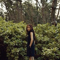 Imutnya Min Hyo Rin berbalut shift dress hitam dengan latar belakang tanaman hijau. Foto: dok. Dazed