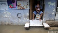 Seorang ayah menggendong bayinya di belakang rumah menunggu banjir surut.