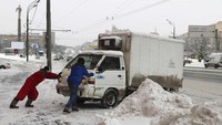 Dua pria tengah mendorong mobil di dekat monumen kosmonot Rusia, Yuri Gagarin, usai hujan salju yang lebat. (Foto: Dok. REUTERS/Sergei Karpukhin)