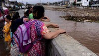 Warga menonton sampah yang terbawa arus banjir di Sungai Ciliwung.