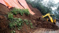 Satu alat berat mengeruk longsoran tanah.