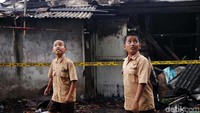 Dua siswa melintasi di depan rumah yang terbakar.