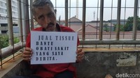 Di tempat ia berjualan di JPO UI, Pak Deden menempel kertas yang dilaminating. Jual tissue bantu obati sakit yang saya derita, tulisnya