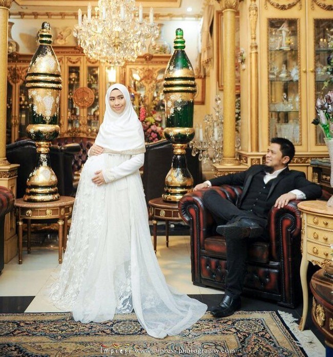 Oki Setiana Dewi juga bergaya ala ratu dan raja bersama suaminya. Ia mengenakan gaun mewah putih dipadukan dengan hijab sifon berwarna senada. Foto ini diabadikan oleh Impresi Fotografi. Foto: Instagram