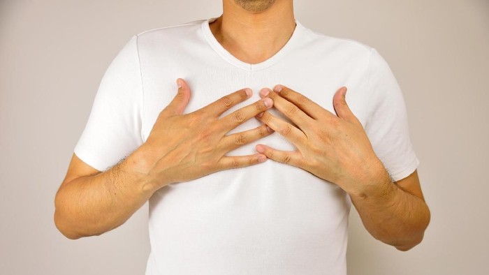 man with both hands on breast because of hard breathing and angina pectoris on grey background