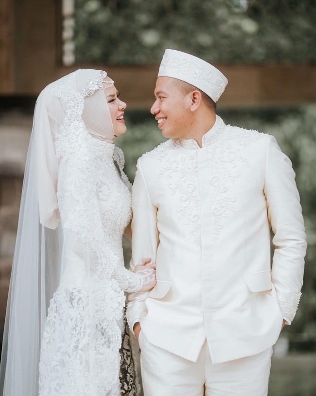 Acara akad nikah diselenggarakan di Masjid Istiqlal Jakarta Pusat. Angel Lelga mengenakan kebaya modern berwarna putih dipadukan dengan kain batik sidomukti. Hijabnya yang simple dibuat spesial dengan tambahan veil bertabur swarovski dan headpiece yang elegan. Foto: Instagram