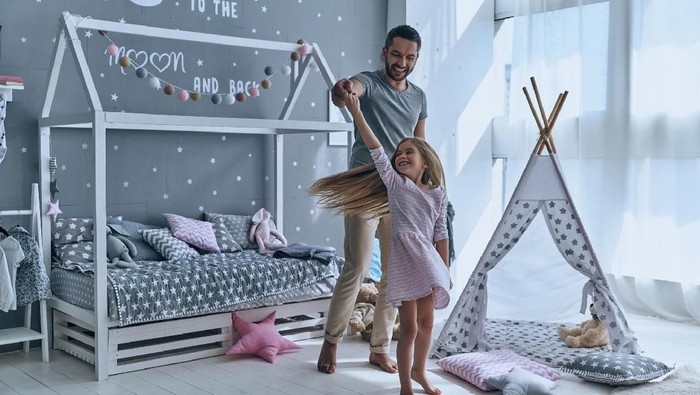 Full length of father and daughter holding hands and smiling while dancing in bedroom