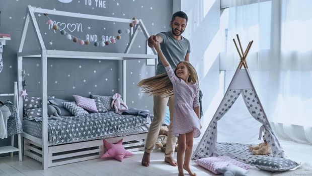 Full length of father and daughter holding hands and smiling while dancing in bedroom