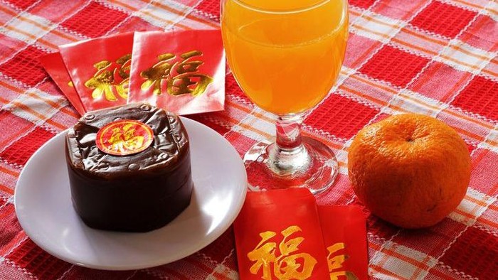 Nian Gao served at the table with a glass of orange juice cupcakes and red packets. image is suitable for food and beverage articles and all design related to the celebration of Chinese New Year