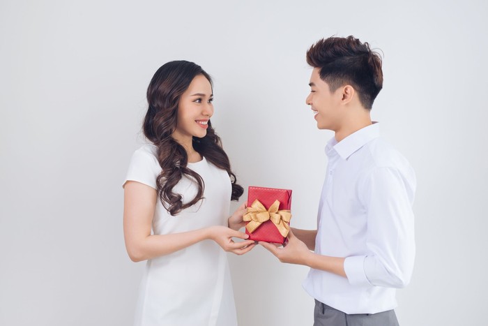 904487580 Love. Handsome young Vietnamese man giving present to beautiful woman at home