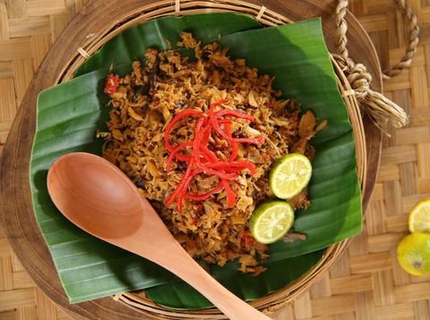 Pampis Ikan Tongkol, a traditional seafood dish from Manado, Sulawesi. Shredded mackerel fish cooked in spicy spice mixture, then garnished with red chili pepper and lime halves. The food is plated on a traditional woven bamboo plate that has been lined with banana leaf; a wooden spoon inserted inside. The plate is then arranged on a woven bamboo tray.