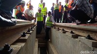 Dengan kemeja putih dibalut rompi proyek hijau menyala, Budi Karya memerhatikan kondisi rel dan saluran air di bawahnya.