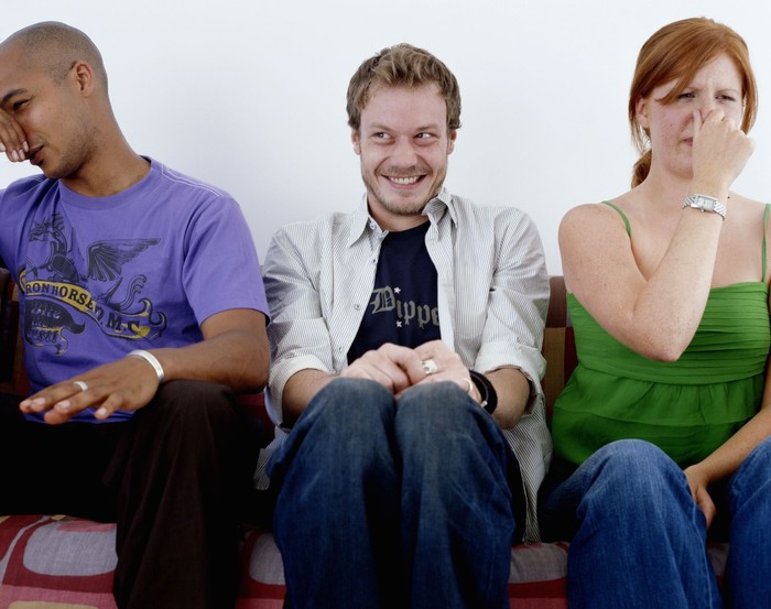 Young man, smiling, sitting between man and woman holding noses