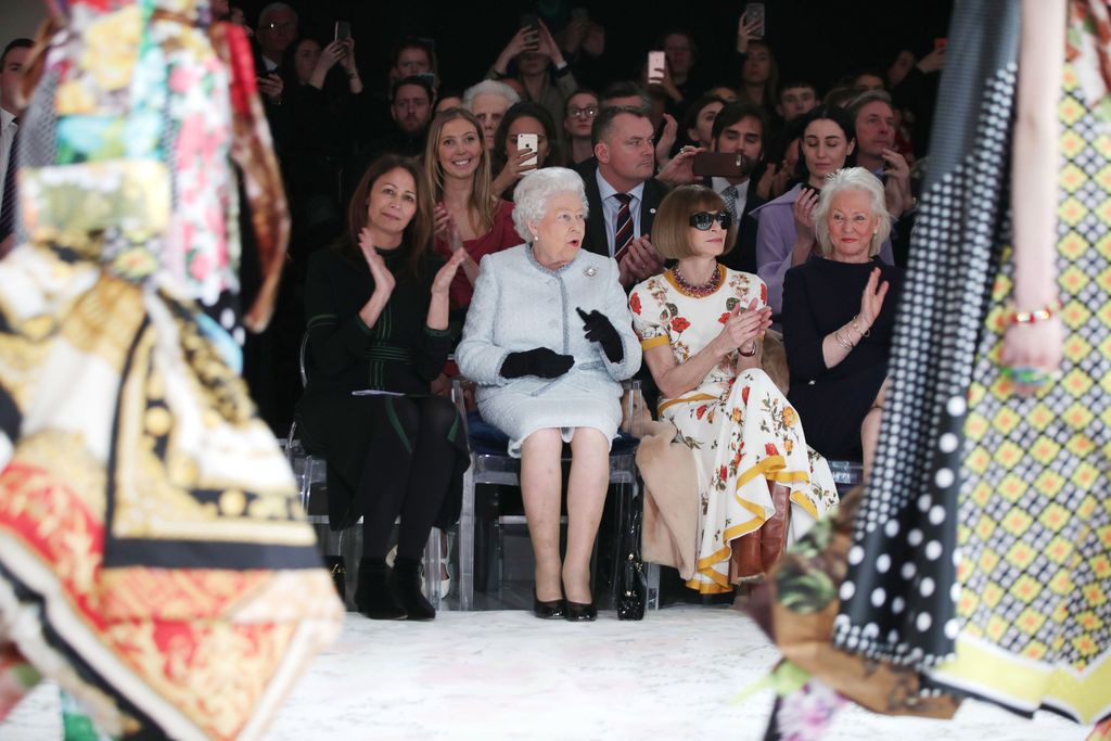 LONDON, ENGLAND - FEBRUARY 20:  Queen Elizabeth II sits next to Anna Wintour (R) and Caroline Rush, chief executive of the British Fashion Council (BFC) (L) as they view Richard Quinn's runway show before presenting him with the inaugural Queen Elizabeth II Award for British Design as she visits London Fashion Week's BFC Show Space on February 20, 2018 in London, United Kingdom. (Photo by Yui Mok - Pool/Getty Images)