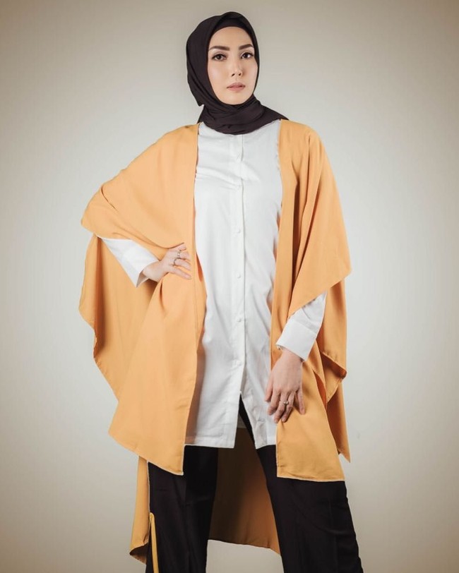 Baru berhijab dan belum punya banyak baju panjang? Atasi dengan pemakaian outerwear. Cardigan atau vest bisa dipadupadankan dengan kaos lengan pendek, atau baju atasan yang terlalu pendek. Fenita Arie memadukan cape oversized dengan kemeja ukuran fit.Foto: Instagram