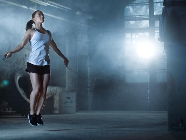 Athletic Beautiful Woman Exercises with Jump / Skipping Rope in a Gym. Shes Covered in Sweat from Her Intense Cross Fitness Training. Dark atmosphere.