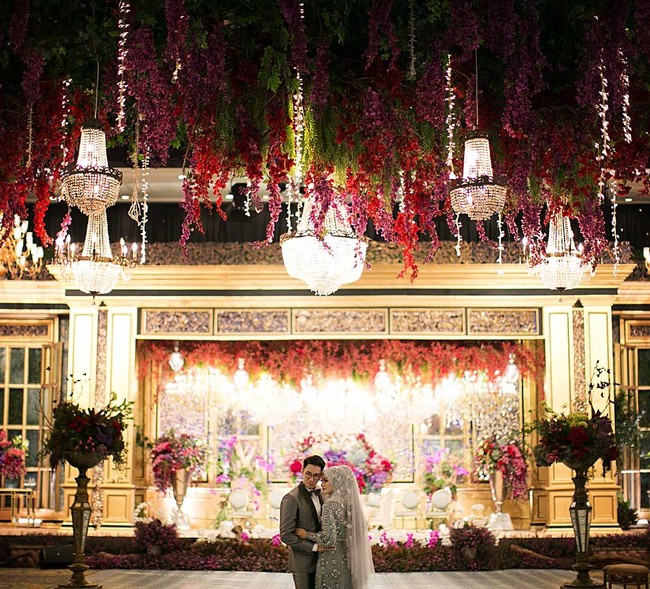 Inilah kemewahan dekorasi pernikahan Mega Iskanti di Jakarta Convention Center. Dekorasi yang ditangani Stupa Caspea itu menghadirkan kemewahan dengan lampu chandelier di area pelaminan dan berbagai bunga bernuansa merah hingga fuschia. Foto: Instagram