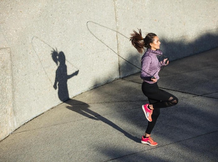 Athletic Beautiful Woman Exercises with Jump / Skipping Rope in a Gym. Shes Covered in Sweat from Her Intense Cross Fitness Training. Dark atmosphere.