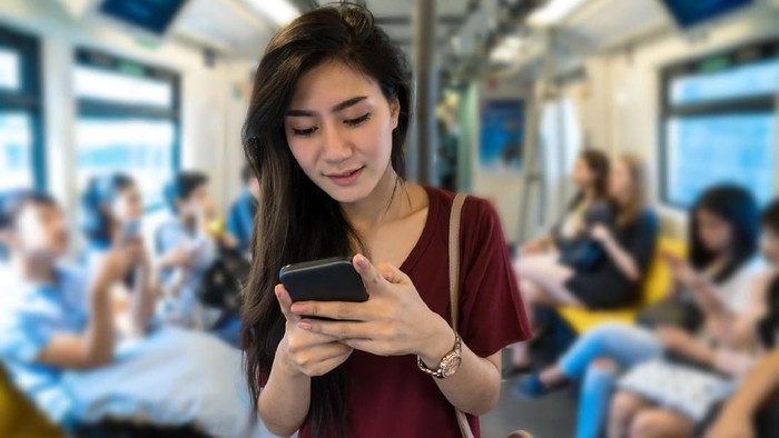 Asian woman passenger with casual suit using the social network via smart mobile phone in the BTS Skytrain rails or MRT subway for travel in the big city, lifestyle and transportation concept