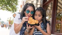 Kalau ini gaya Angie dan putrinya melahap waffle Mickey di Hong Kong Disneyland. Dua-duanya kelihatan cantik! Foto: Instagram novitaangie