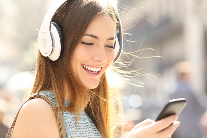 earphone Portrait of a happy girl listening music on line with wireless headphones from a smartphone in the street in a summer sunny day