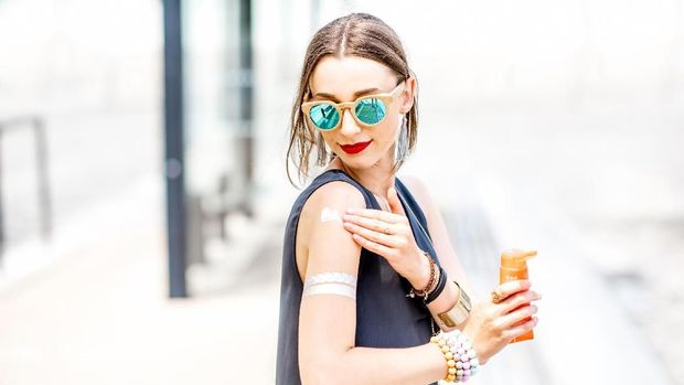 Young woman applying sunscreen lotion standing outdoors at the urban location during the sunny weather