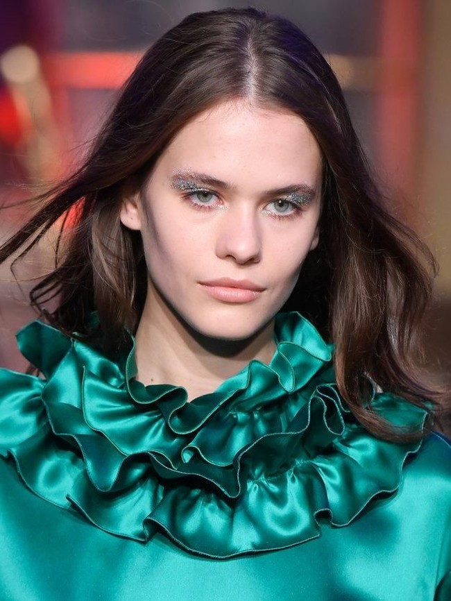 Tak cukup dengan riasan shimmery. Untuk memberikan nuansa yang lebih festive, fashion show Genny menampilkan model dengan riasan mata glitter.  Foto: Getty Images