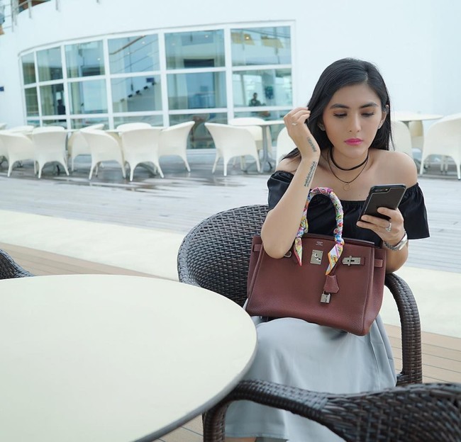 Duduk di restoran sambil melihat ponselnya, Angela Lee terlihat memangku tas Hermes Birkin berwarna merah marun yang pada bagian pegangan tasnya dihiasi scarf Hermes. Tas Hermes tersebut harganya diperkirakan Rp 250 jutaan. Foto: Instagram
