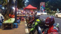 Sejumlah motor dan mobil terparkir di pinggir jalan. Ada tukang parkir yang mengatur di lokasi.