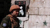 Seorang tentara Rusiah berjalan di depan poster Bashar al-Assad. REUTERS/Omar Sanadiki.