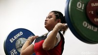Seorang lifter putri berusaha mengangkat beban.