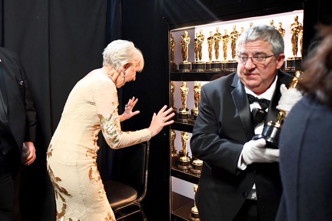 Kelakuan konyol Helen Mirren di depan lemari berisi Piala Oscar. I want all that trophy!! Foto: Getty Images