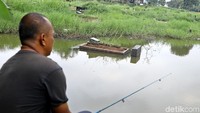 Seorang warga memancing di pemakanan yang terendam air.