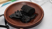 Sekilas sajian ini nggak bisa dimakan ya? Seperti arang gosong. Tapi ini adalah kambing guling lho. Pelengkapnya singkong rebus dan keripik beras berwarna hitam legam. Foto: Istimewa