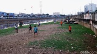 Sejumlah anak bermain sepakbola di pinggir sungai.