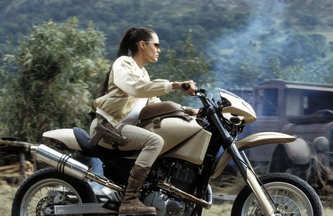 Ini gaya Angelina Jolie saat mengendarai motor di film pertama Tomb Raider. Ia mengenakan setelan warna putih dengan rambut yang kuncir tinggi. Foto: Pinterest