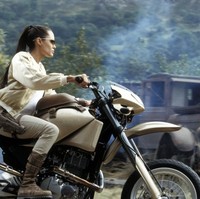 Ini gaya Angelina Jolie saat mengendarai motor di film pertama Tomb Raider. Ia mengenakan setelan warna putih dengan rambut yang kuncir tinggi. Foto: Pinterest