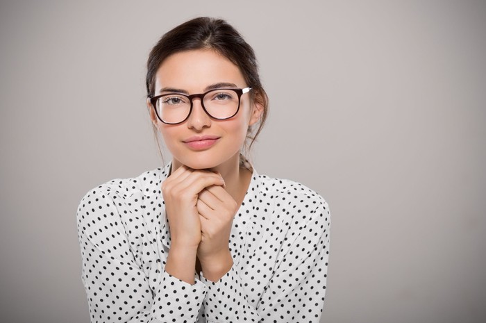 Young woman wearing modern eyeglasses anf thinking isolated on grey background with copy space. Portrait of smiling fashion student wearing big glasses. Proud young businesswoman with spectacles looking at camera.