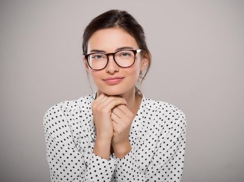 Young woman wearing modern eyeglasses anf thinking isolated on grey background with copy space. Portrait of smiling fashion student wearing big glasses. Proud young businesswoman with spectacles looking at camera.